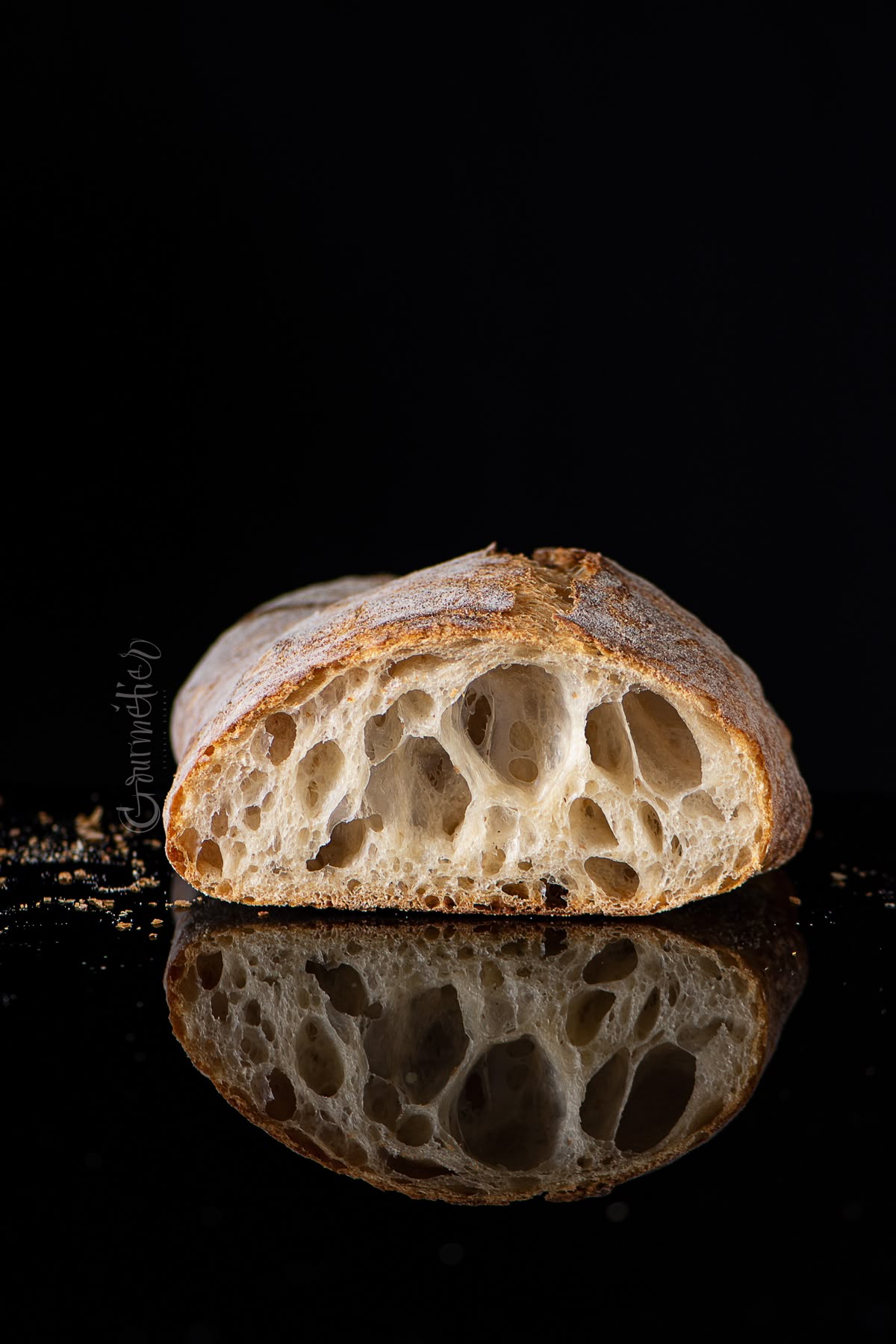 A loaf cut through to show an open, irregular crumb, against a dark background
