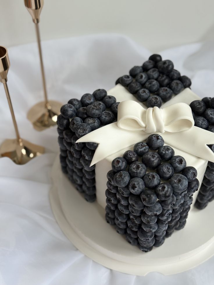 A square cake covered in blueberries, finished with a white ribbon bow