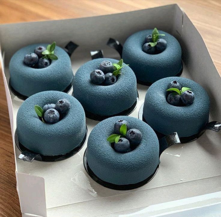 Six small round cakes with a deep blue finish, each topped with blueberries